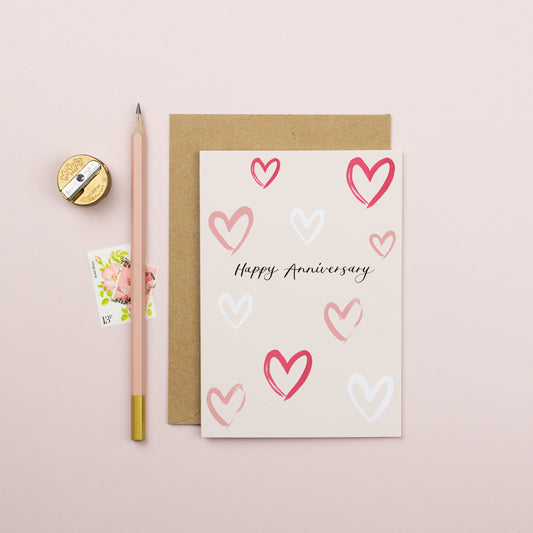 Different shape hearts scattered across the card with happy anniversary text written in modern calligraphy in the middle in black. 