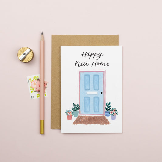A new home card with a blue front door and flower pots either side of the door. The lettering is in modern calligraphy and reads ' happy new home'. 