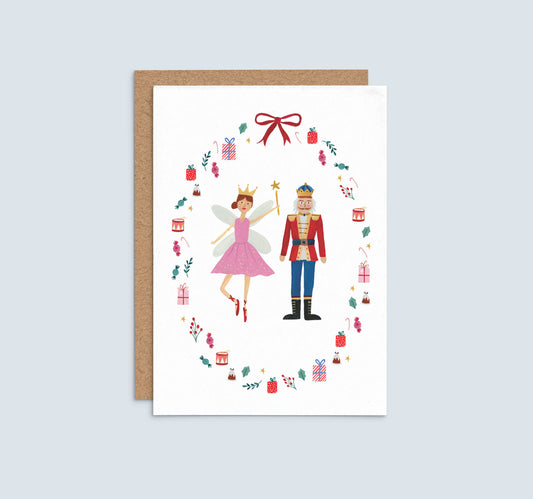 A sugarplum fairy and nutcracker surrounded by presents, sweets and cake in a wreath